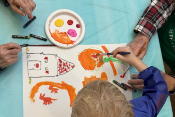 young child and senior adult shown painting a picture