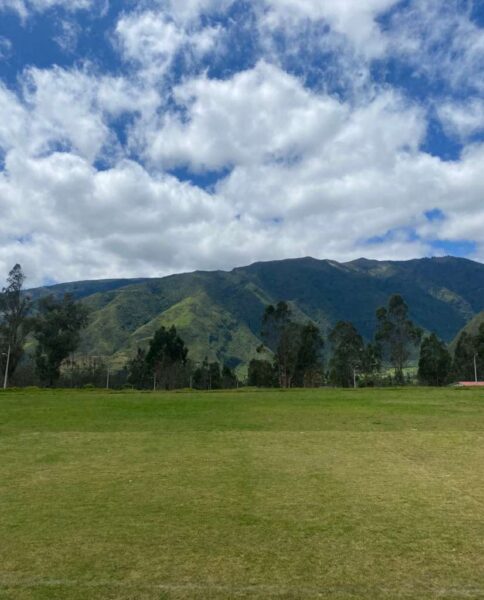 Green mountains rise beneath a partly cloudy sky in the Ecuadorian countryside.