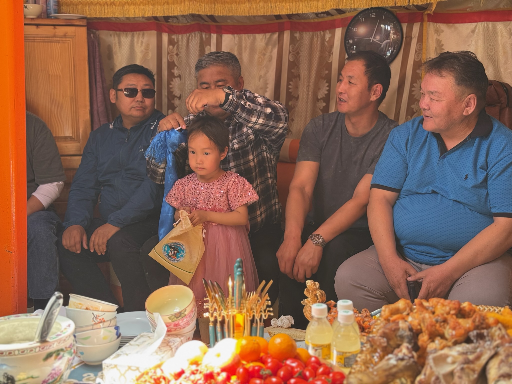 Family members celebrate a young girl's birthday inside a traditional Mongolian ger as she receives a ceremonial gift during the celebration.