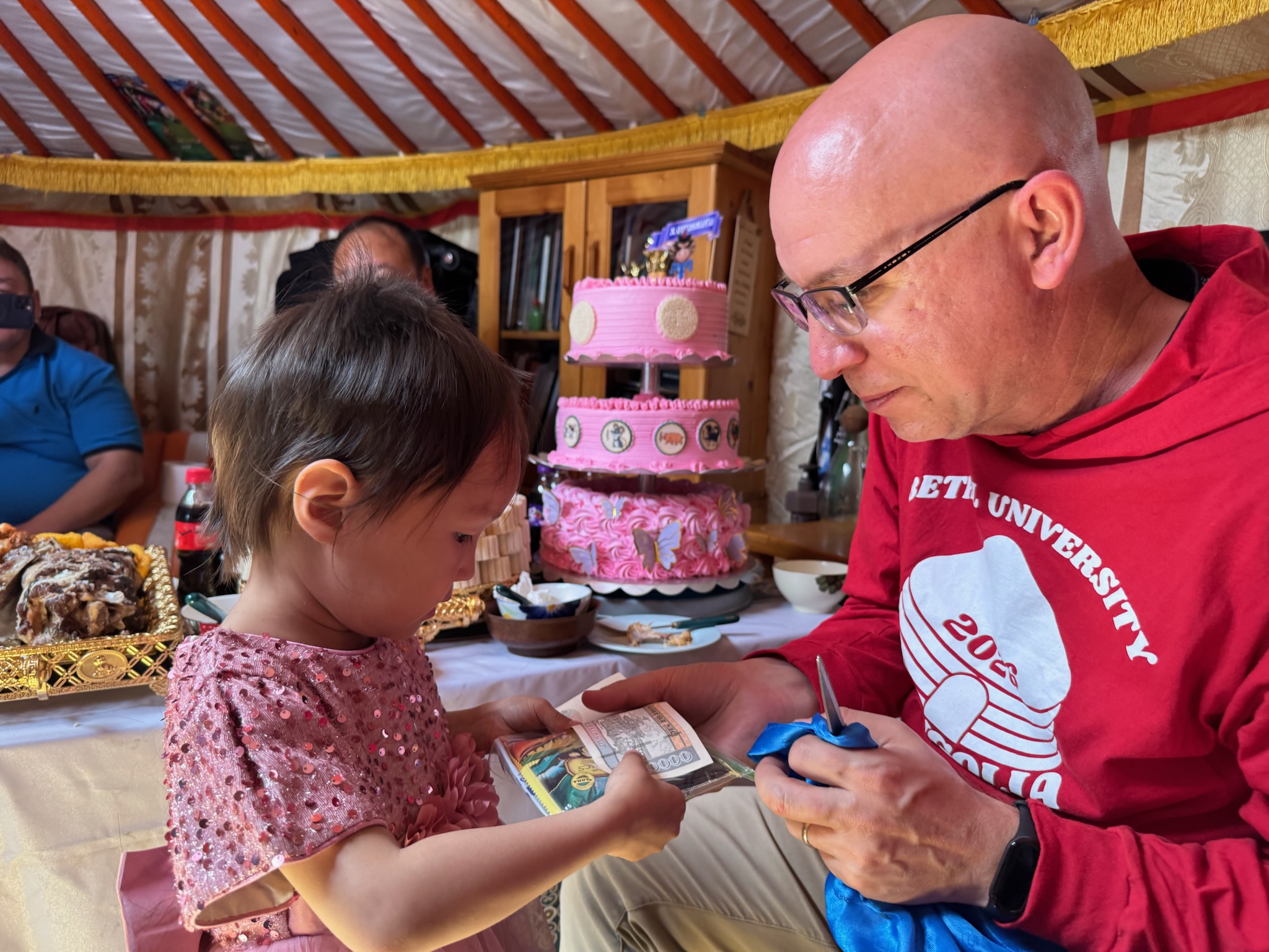 A Bethel University Task Force member presents a birthday gift to a young child during a family celebration inside a traditional Mongolian ger.