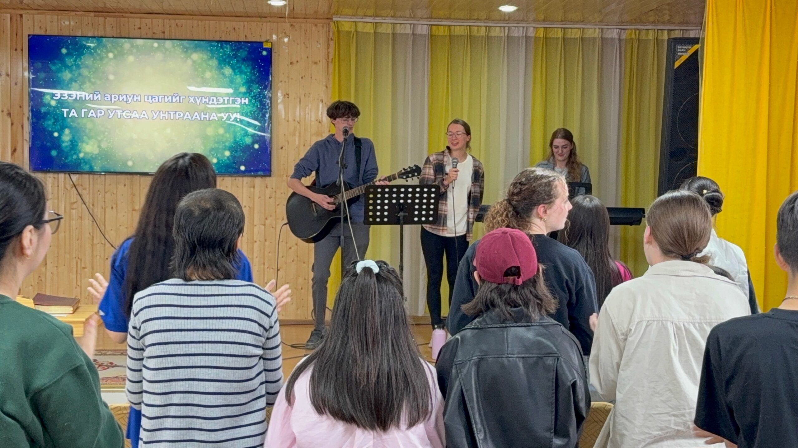 Bethel University students lead worship with music and singing during a church service in Mongolia while the congregation stands together.