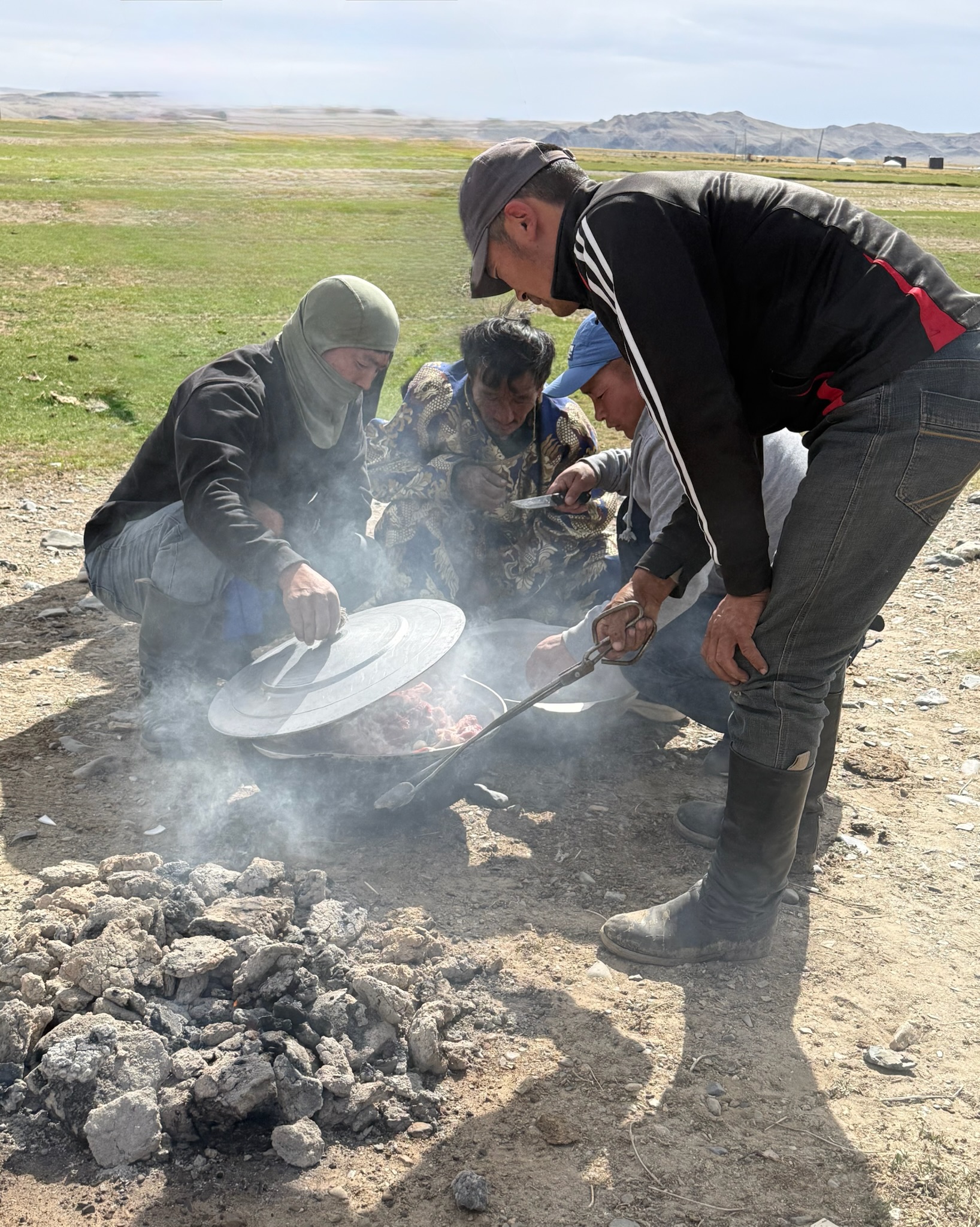 Mongolian families cook a traditional meal outdoors over hot coals while Bethel University Task Force members observe and visit together.