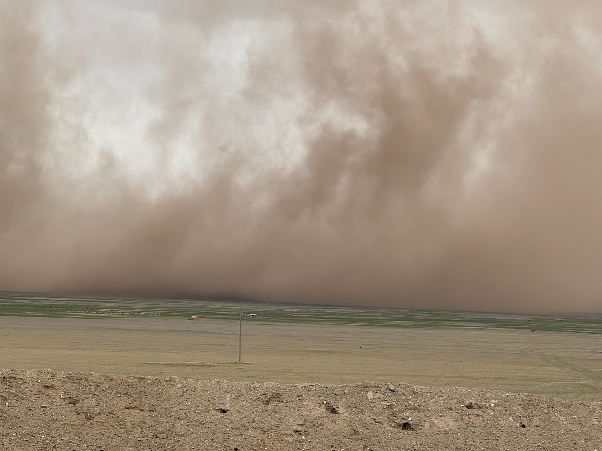 A dramatic dust storm advances across the Mongolian countryside beneath dark swirling clouds.