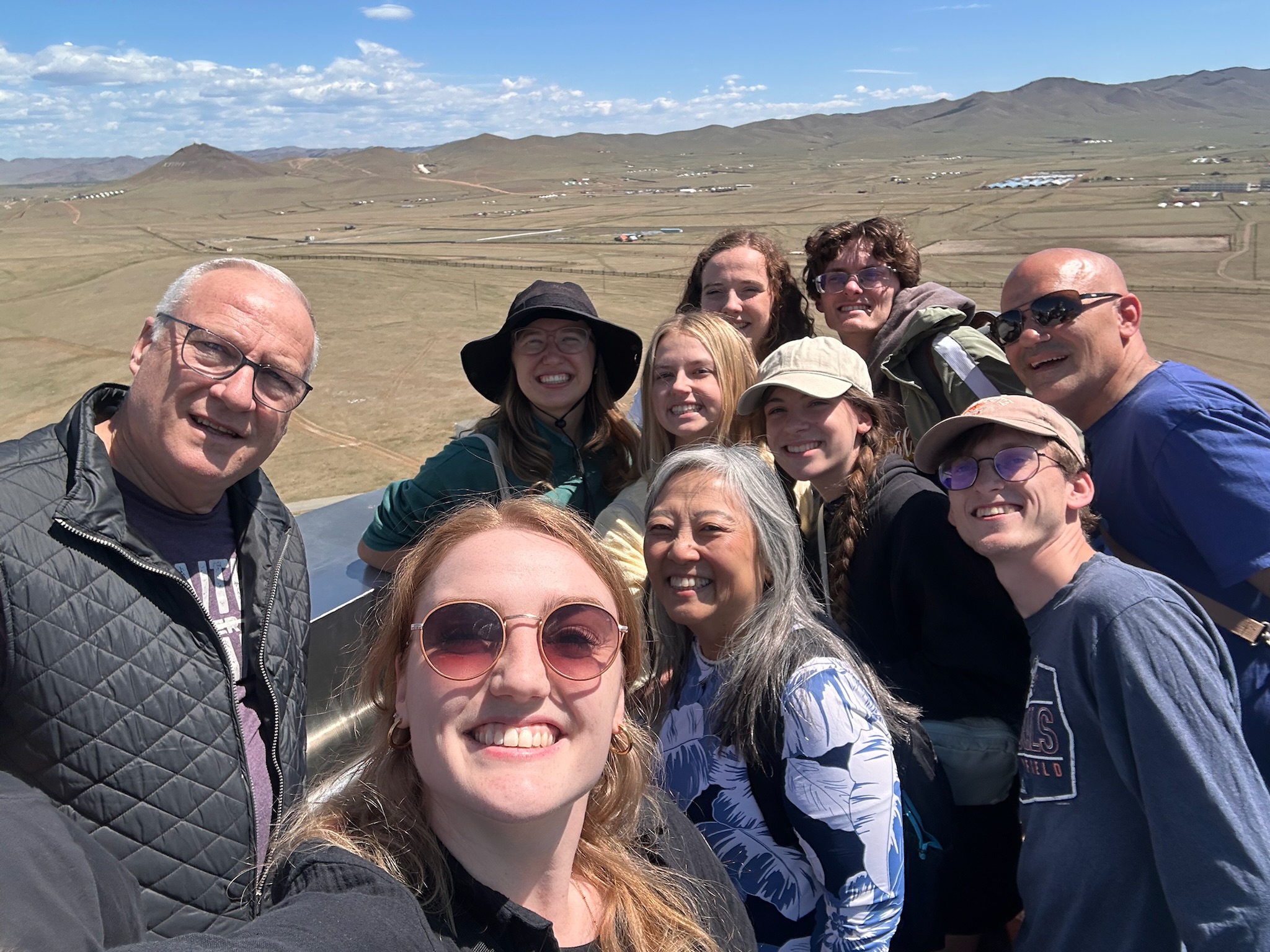 Bethel University Mongolia Task Force members smile together at a scenic overlook with the Mongolian countryside and mountains stretching into the distance.