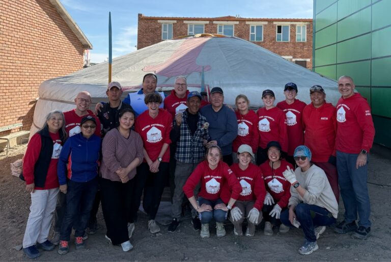 Bethel University students, staff and Mongolian ministry partners pose together in front of a completed ger between two buildings in Mongolia.
