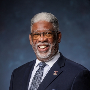 Lynn Coleman ’15, Bethel University’s 2026 Alumnus of the Year, smiling in a professional portrait while wearing a dark suit and patterned tie.