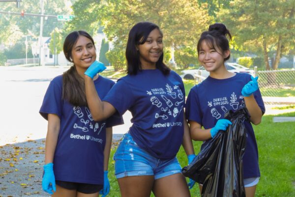 Three Bethel University students wearing Service Day shirts and gloves volunteer in a Mishawaka neighborhood during the 2025 Bethel University Service Day.